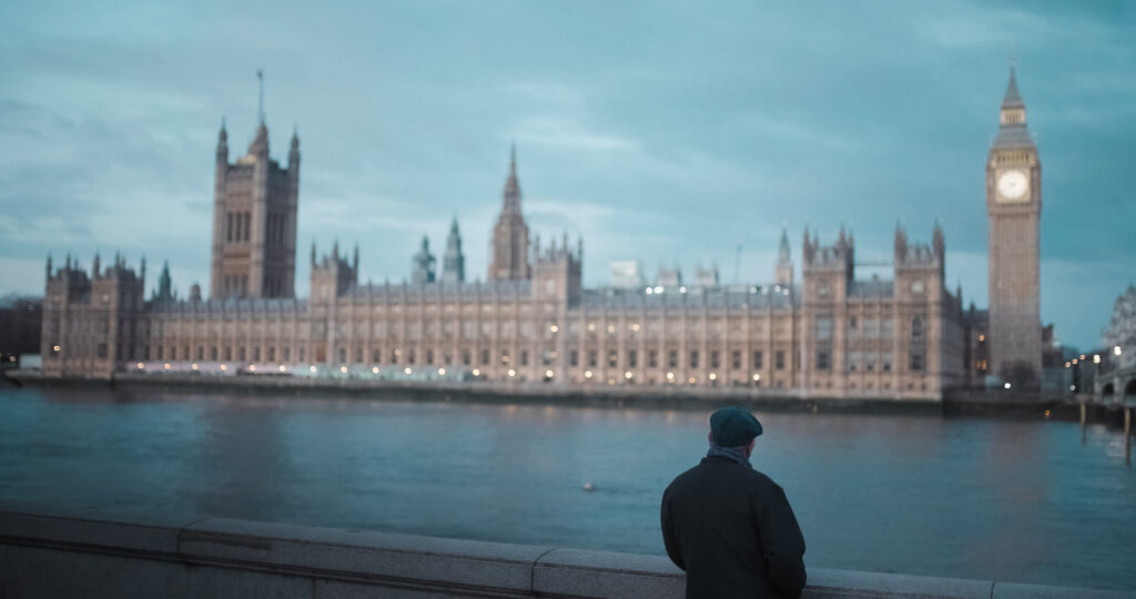 En man i keps står framför parlamentshuset och Big ben i London.