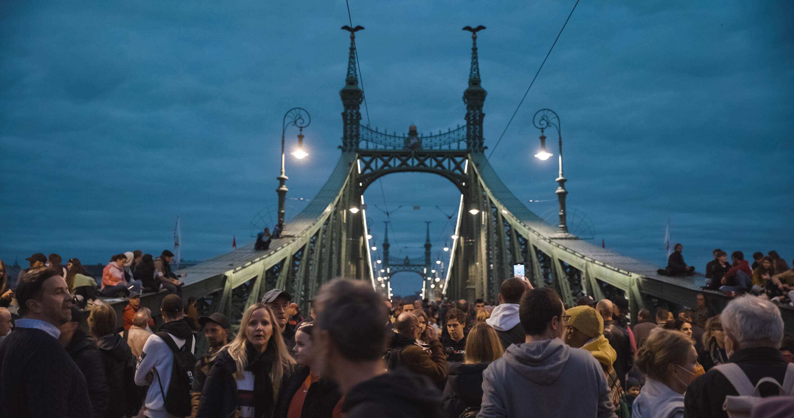 Demonstrandet på en gammal bro i Budapest. Det är kväll och lampor på bron lyser.