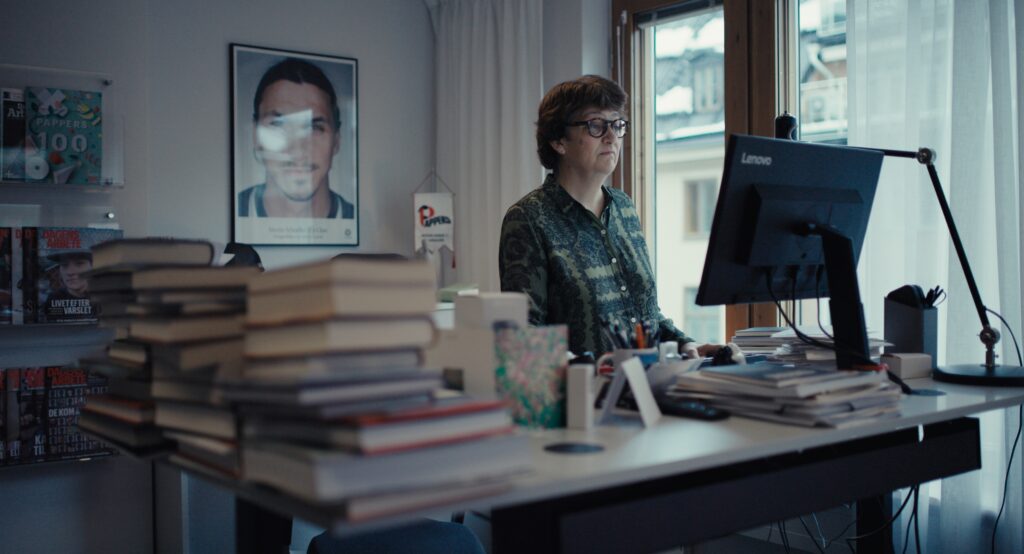 En kvinna står och jobbar vid en dator på ett kontor. Det är många böcker på skrivbordet.