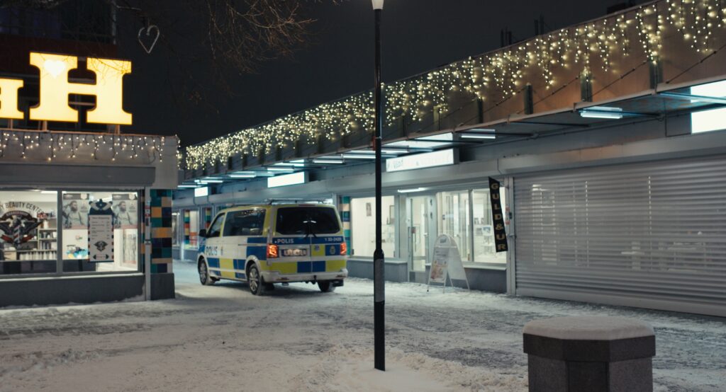 Polisbil åker mellan butiker på ett torg i en förort